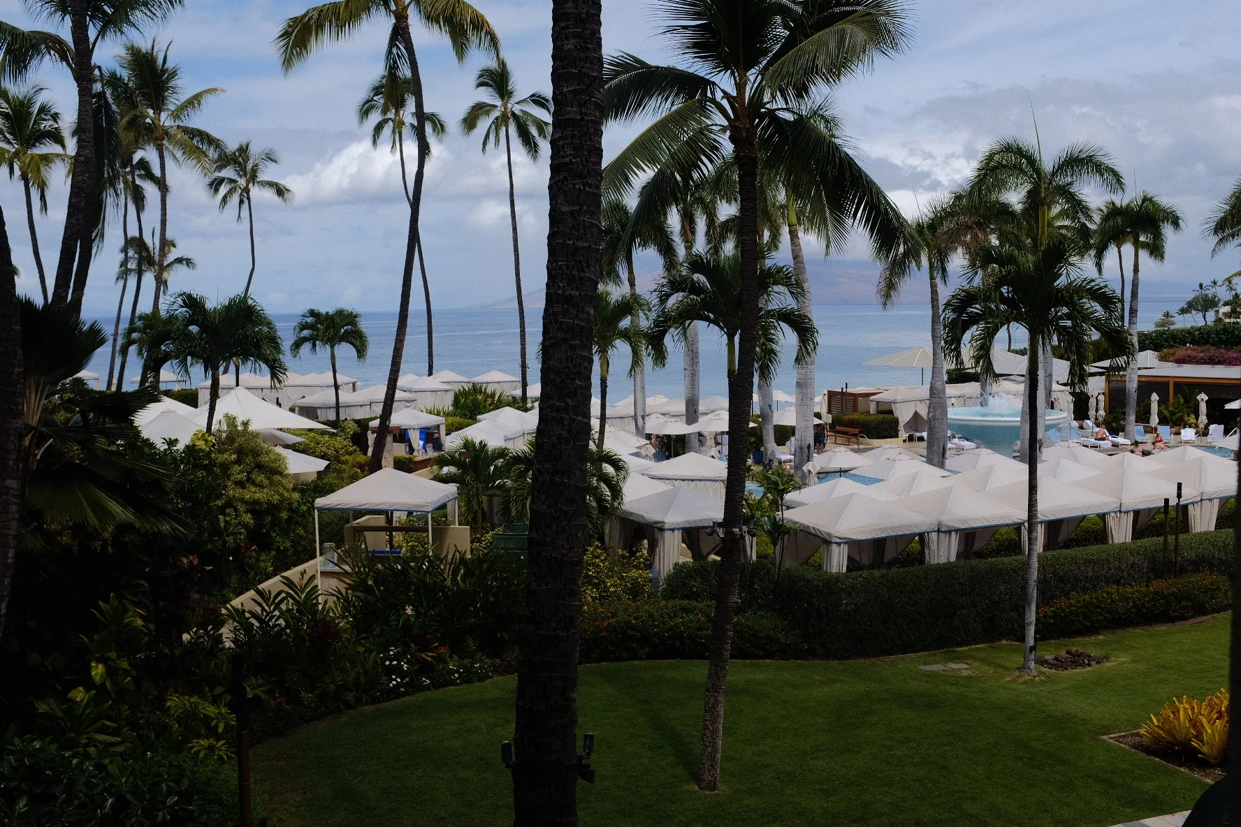 Resort lawn and white cabanas framed by coconut palms above the sea