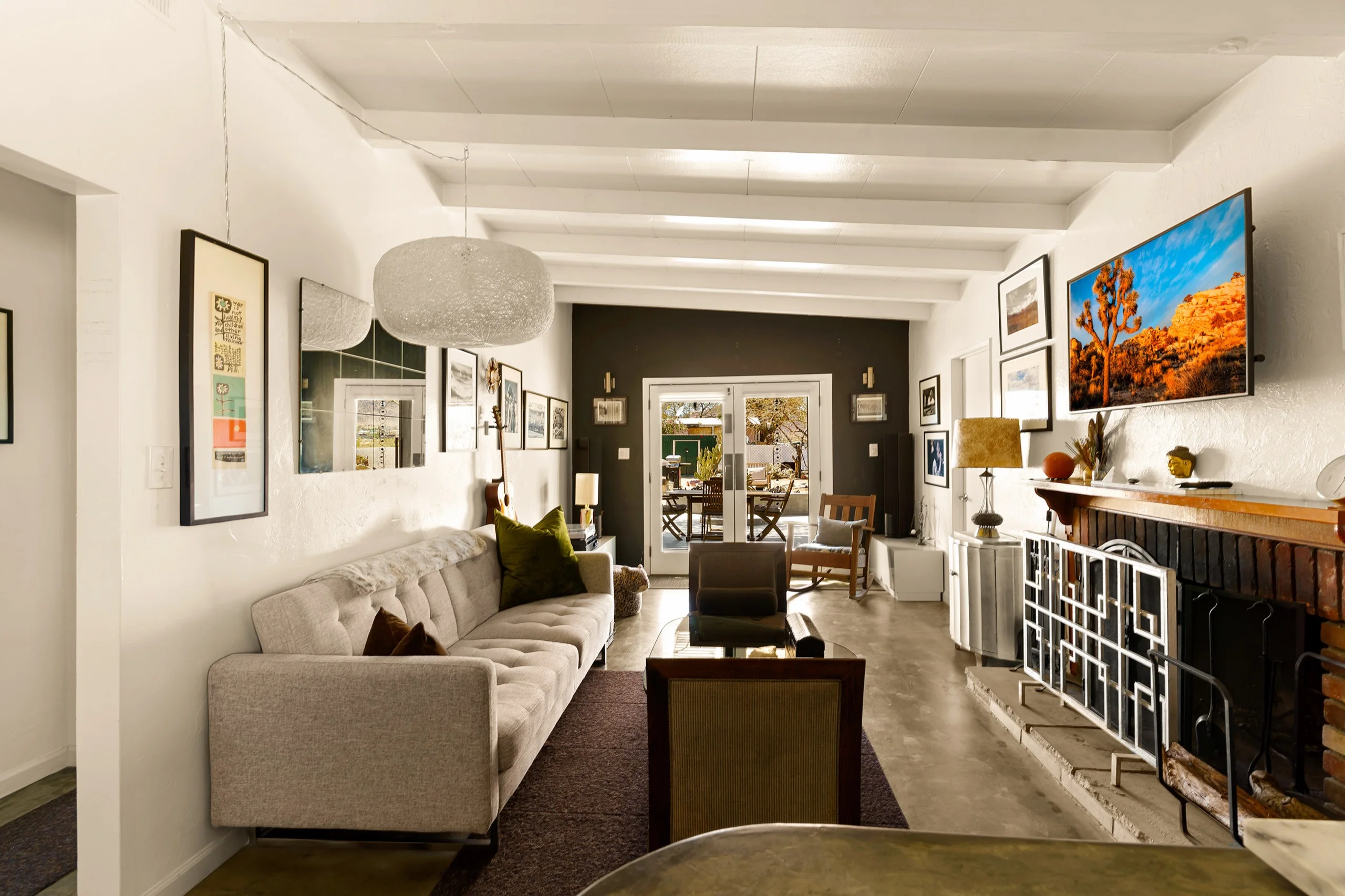 Long living room under white beams, framed prints along both walls and a fireplace at the far end