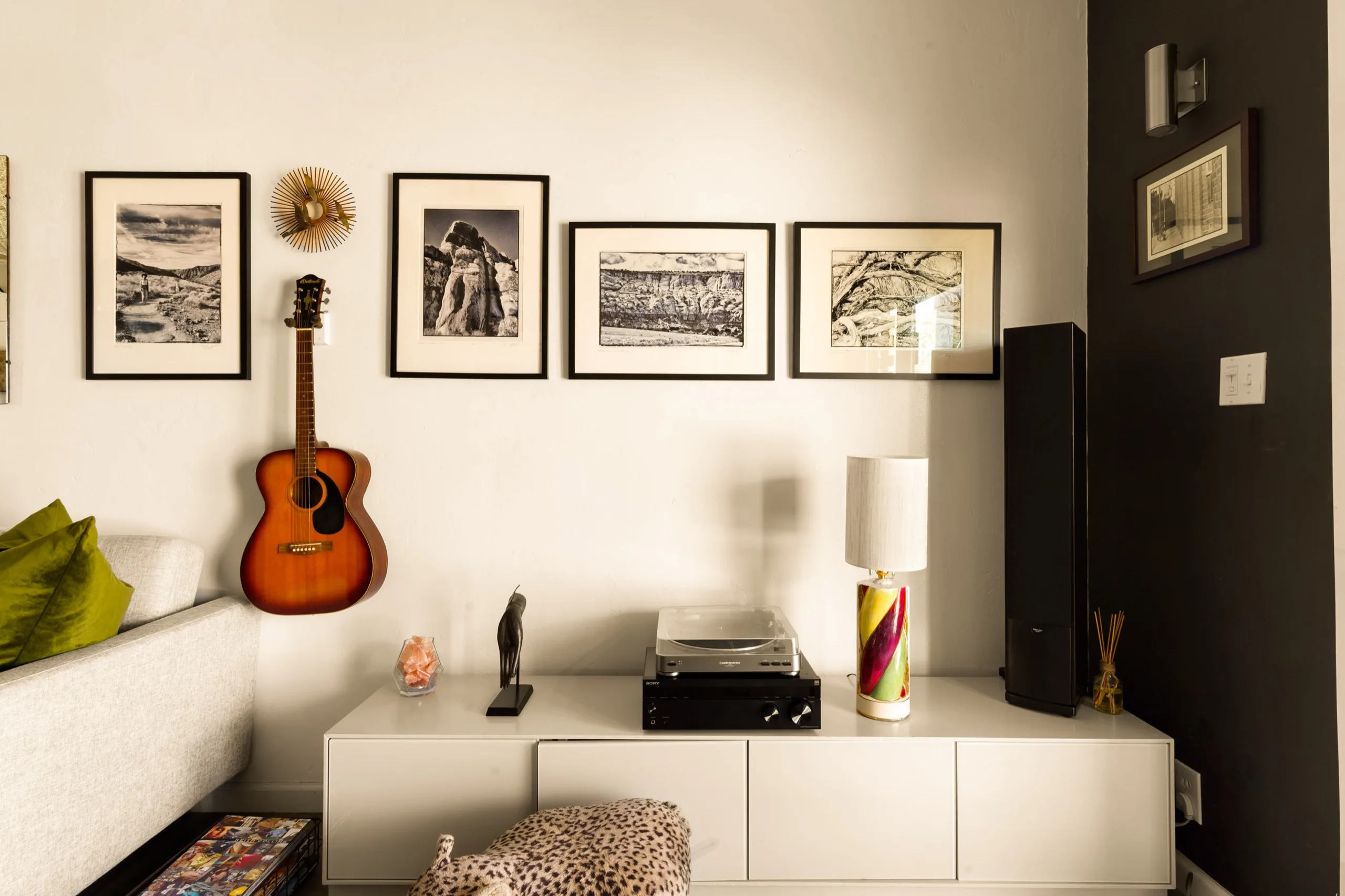Guest room vignette with a row of framed black-and-white prints, an acoustic guitar and a record player