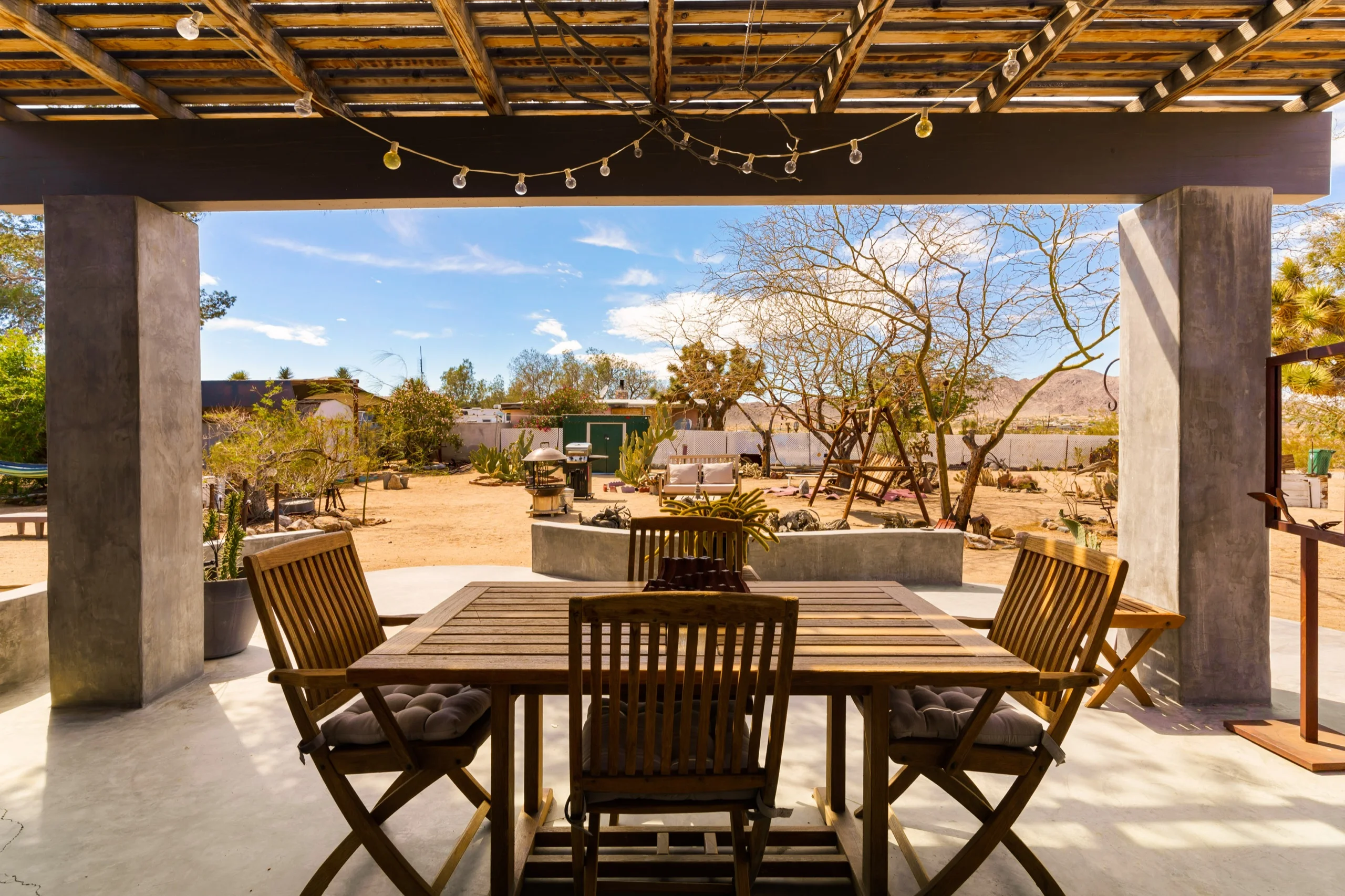 Ocotillo-shaded pergola over a concrete terrace, a dining table set out to the desert yard beyond