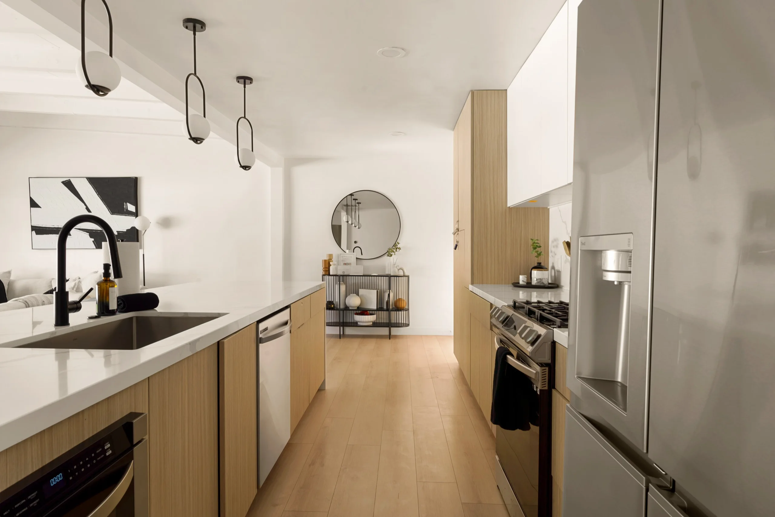 Narrow galley kitchen in pale oak and white stone, blackened tap and pendant lights