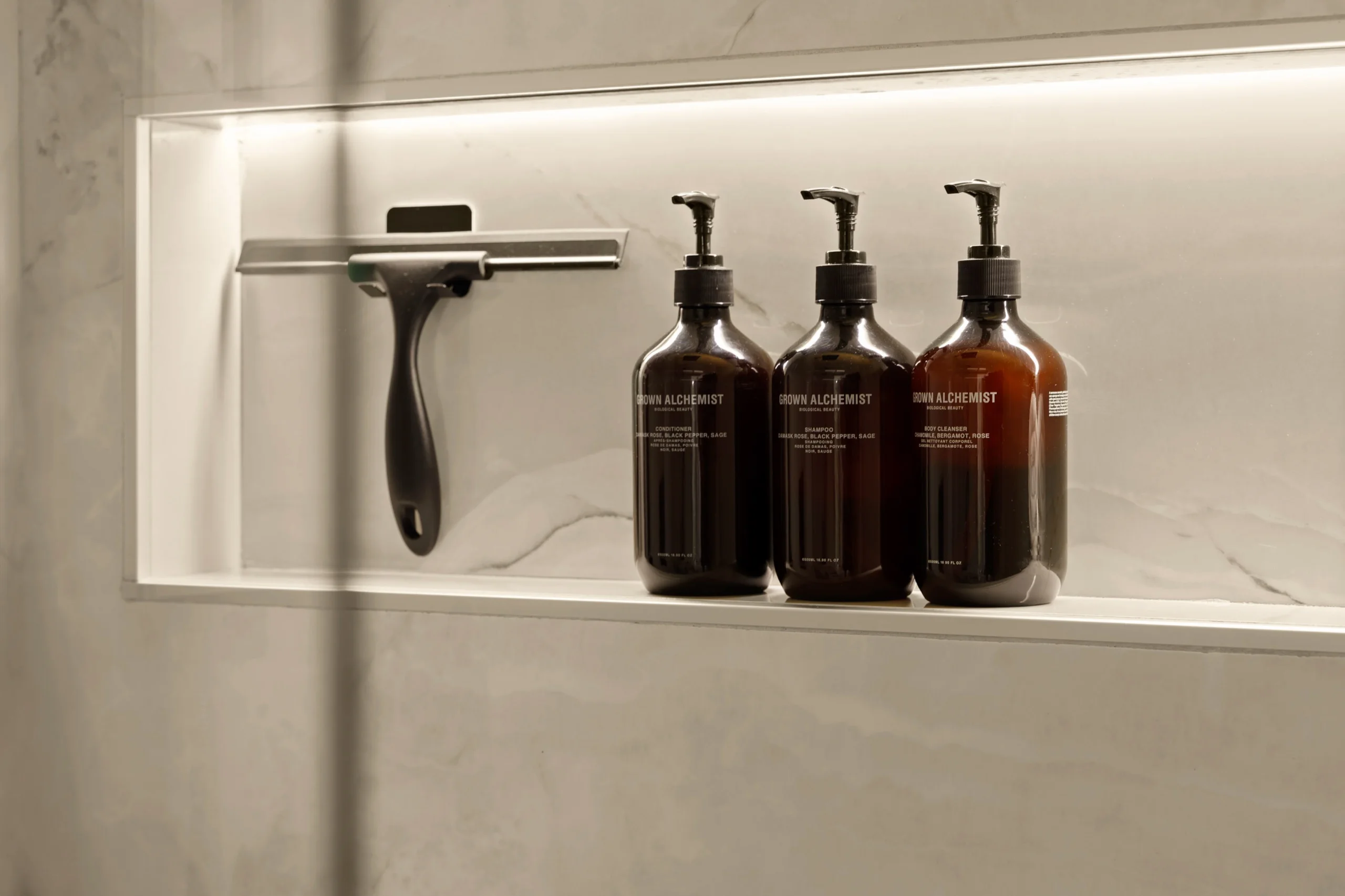 Lit stone shower niche holding three amber apothecary bottles and a chrome razor