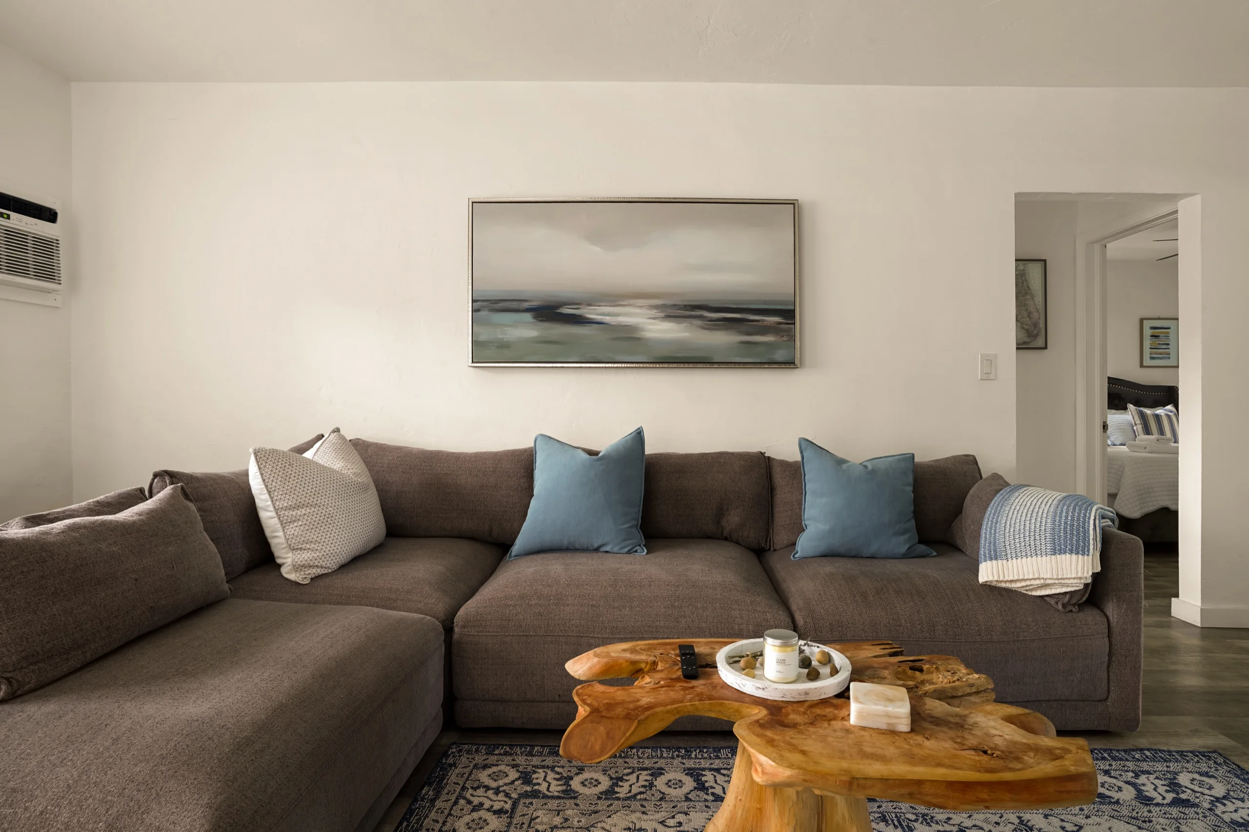 Living room with a deep brown sectional, a live-edge timber table and a soft seascape hung above it
