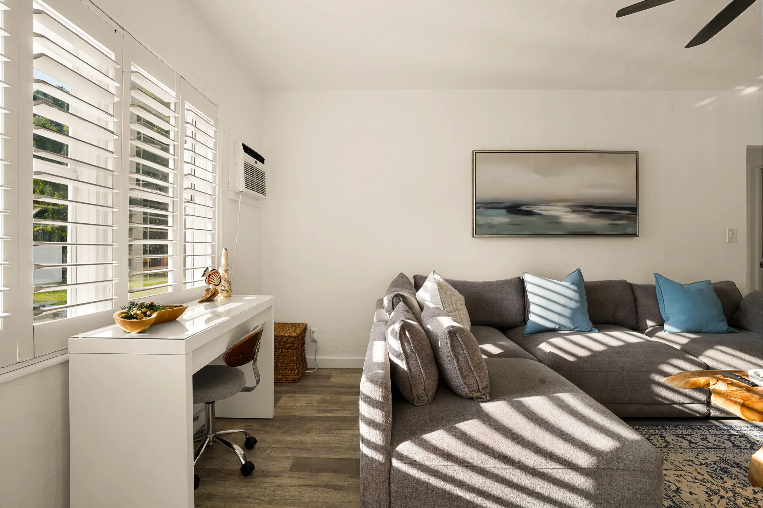 Corner of the living room with a writing desk at the shuttered window and the grey sectional alongside