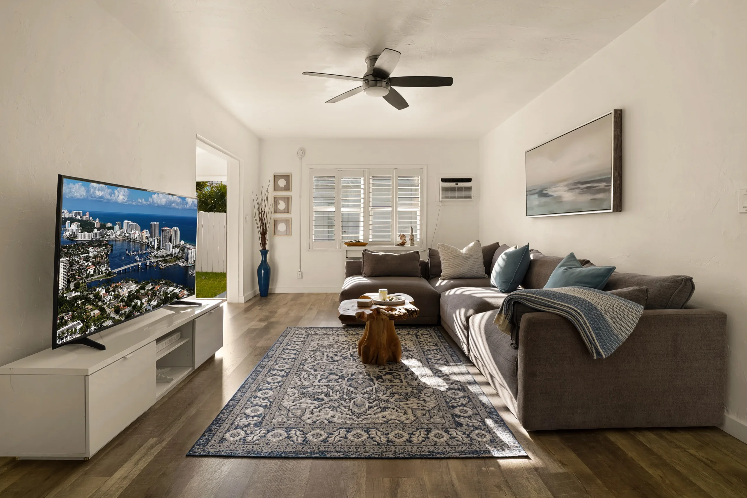 Living room in late sun, grey sectional along two walls, blue patterned rug and a live-edge stump table