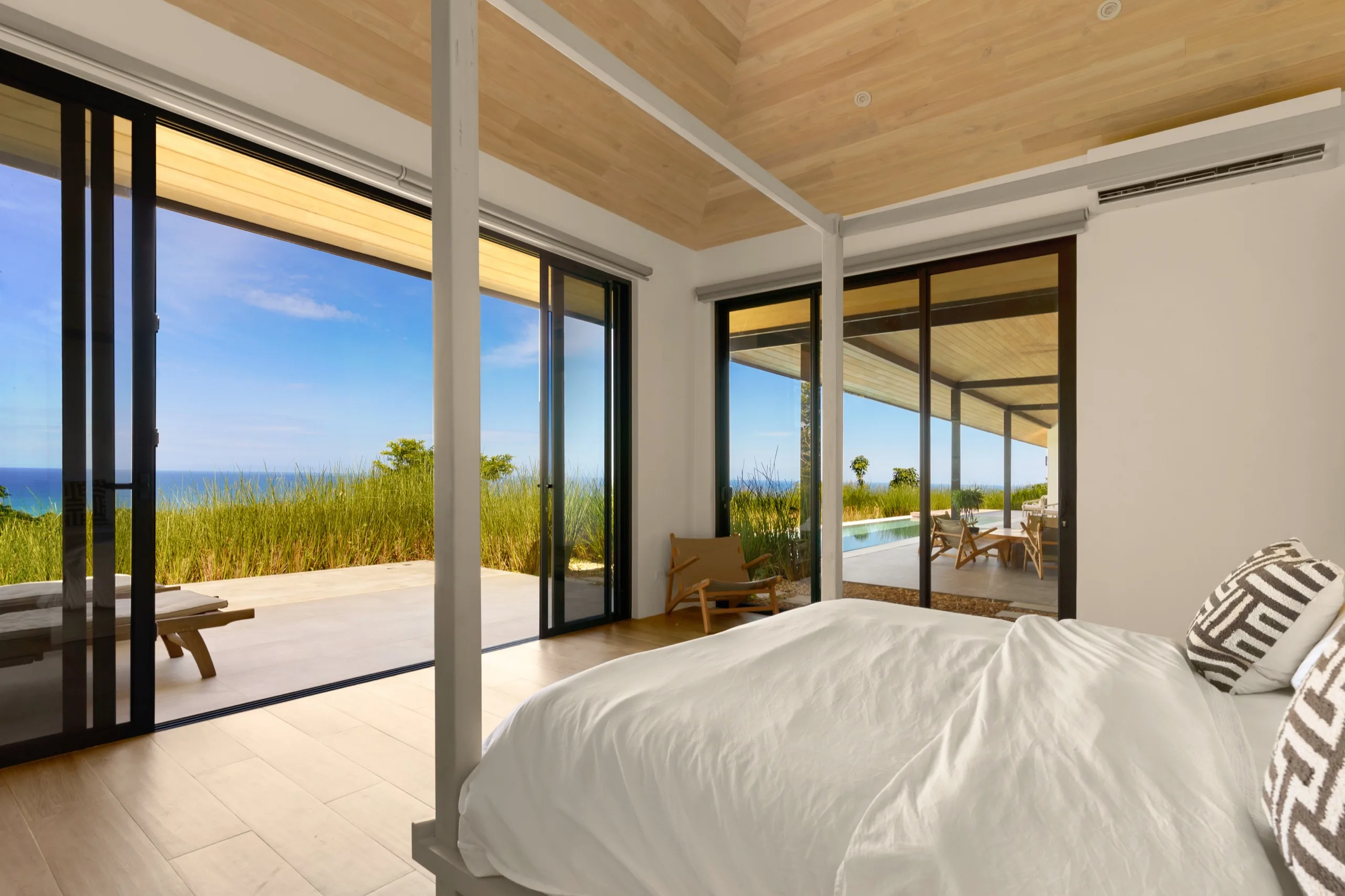 Corner bedroom opening on two sides to the pool terrace, dune grass and the sea beyond