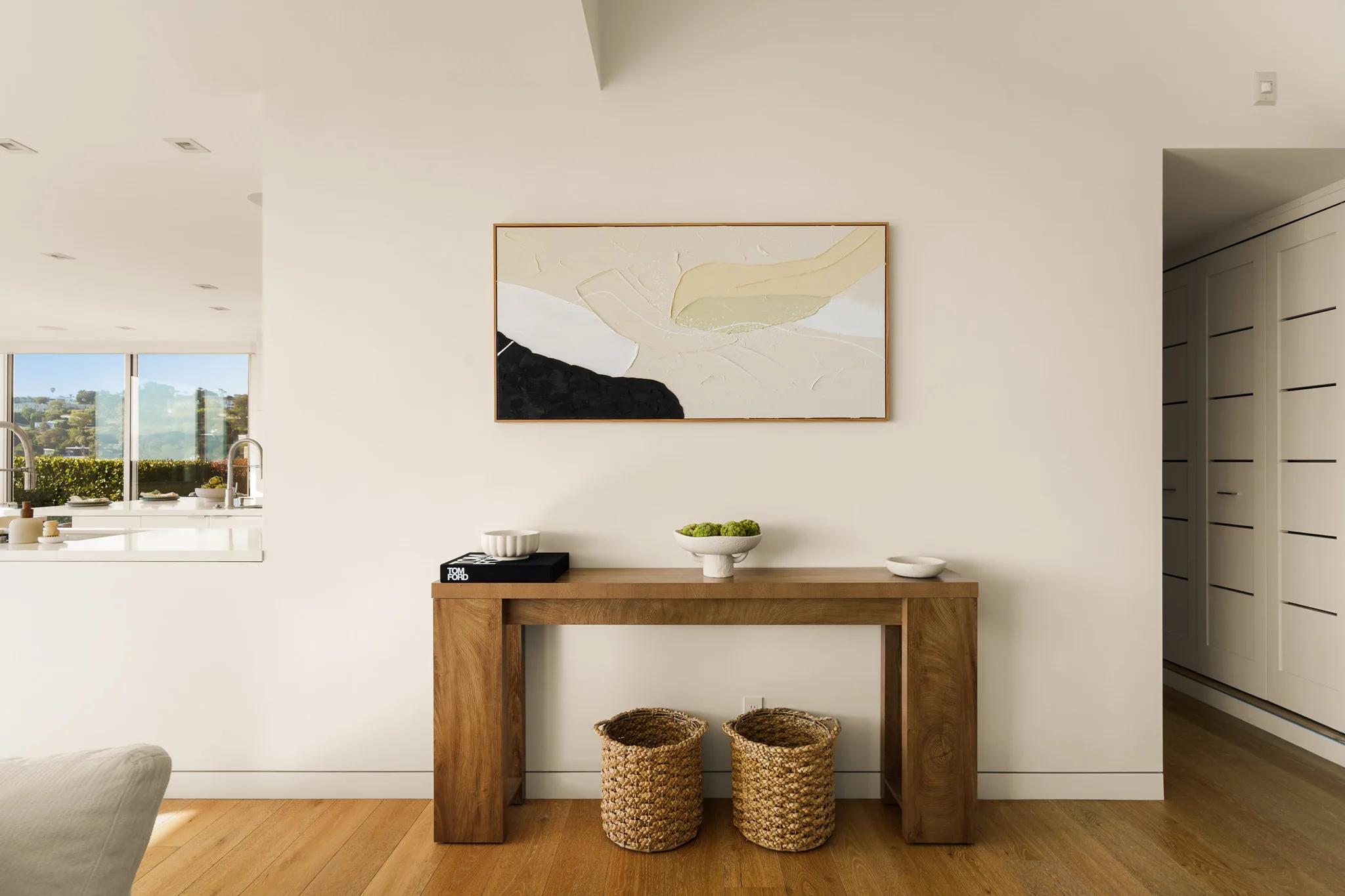 Solid oak console table below a large abstract canvas, woven baskets tucked beneath