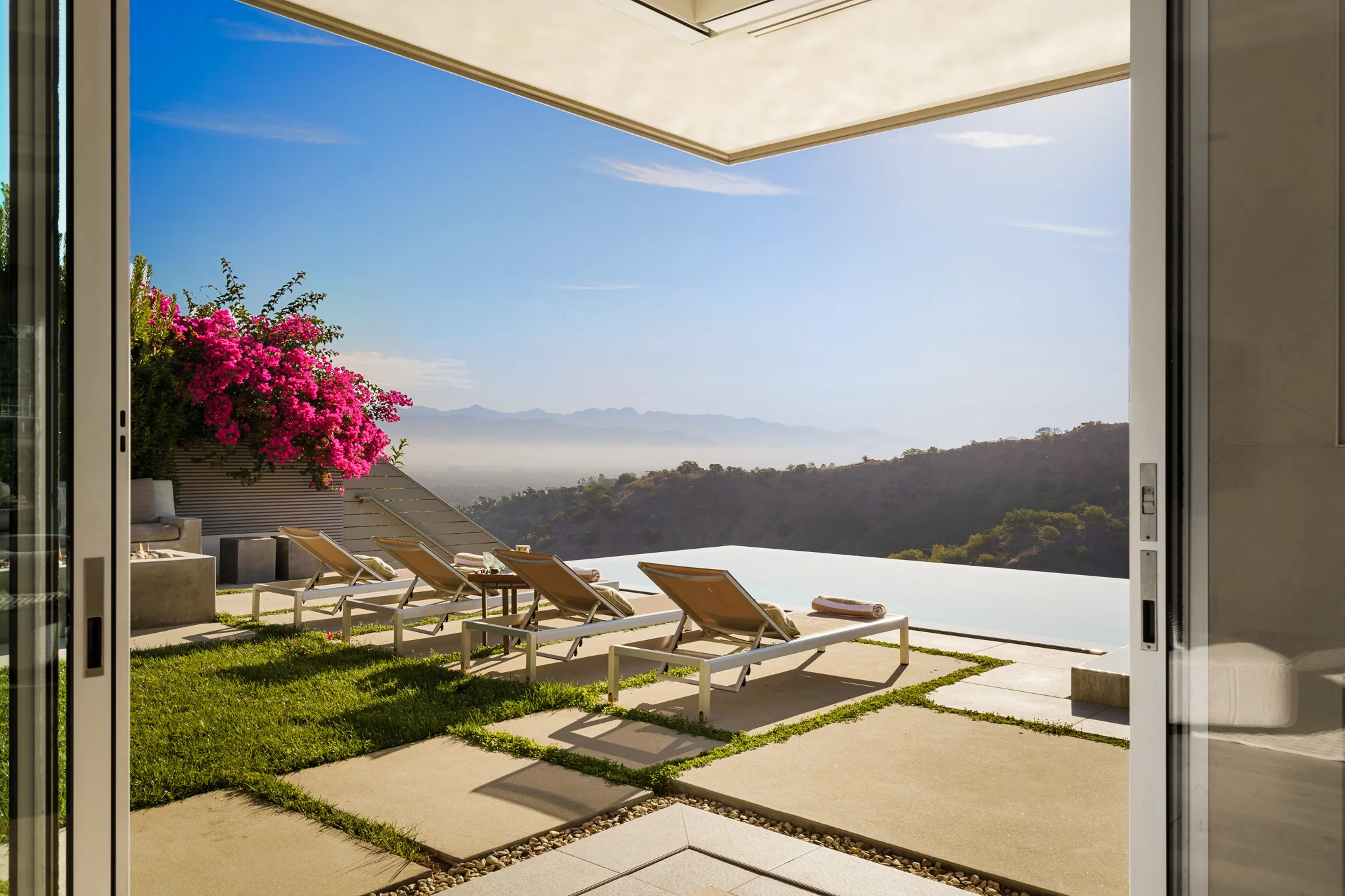 Sliding doors open to loungers at the pool edge, bougainvillea in bloom and the basin hazy below