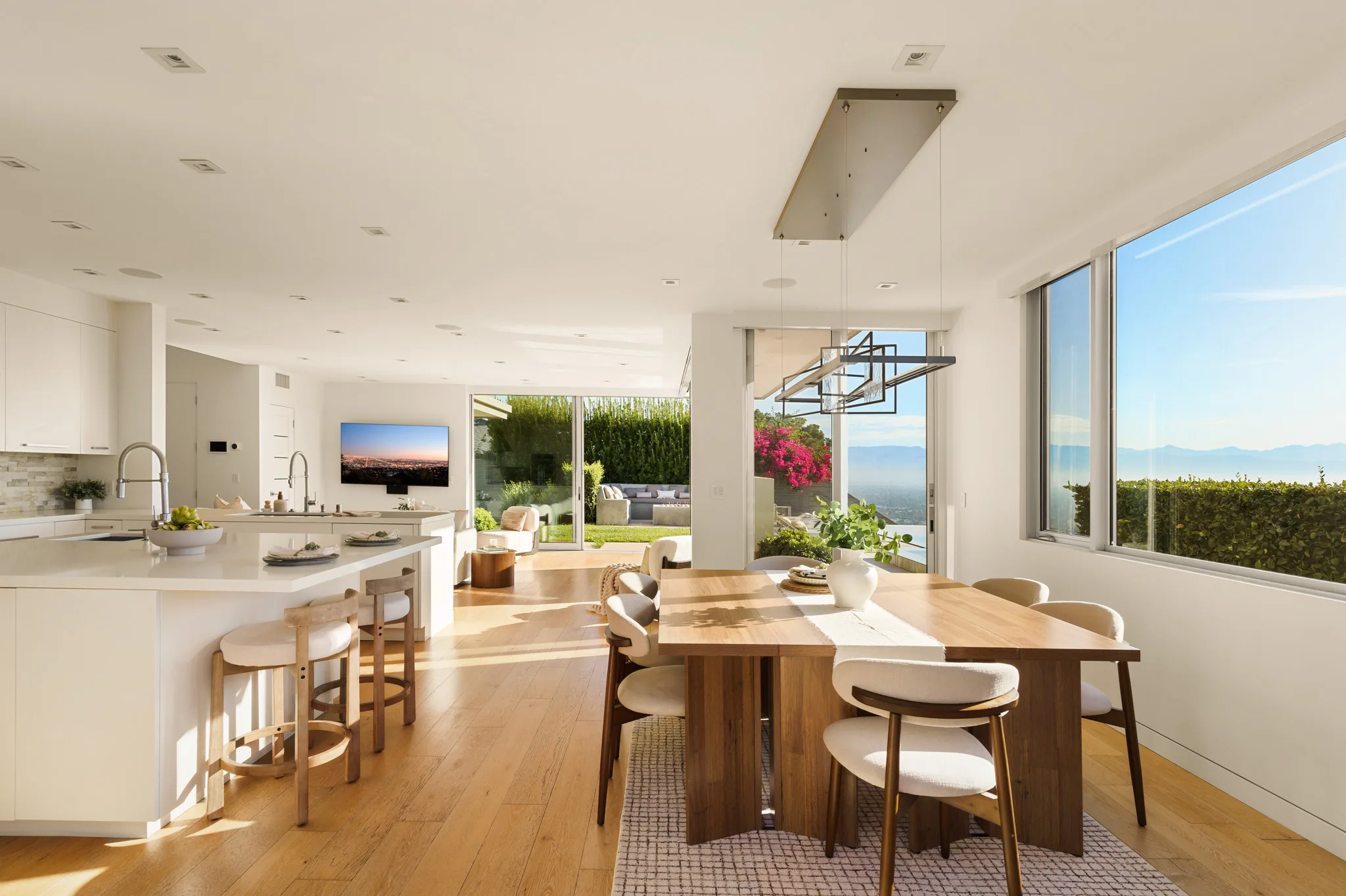 Open kitchen and dining table beneath a wall of glass, pale island and counter stools, hills through every window