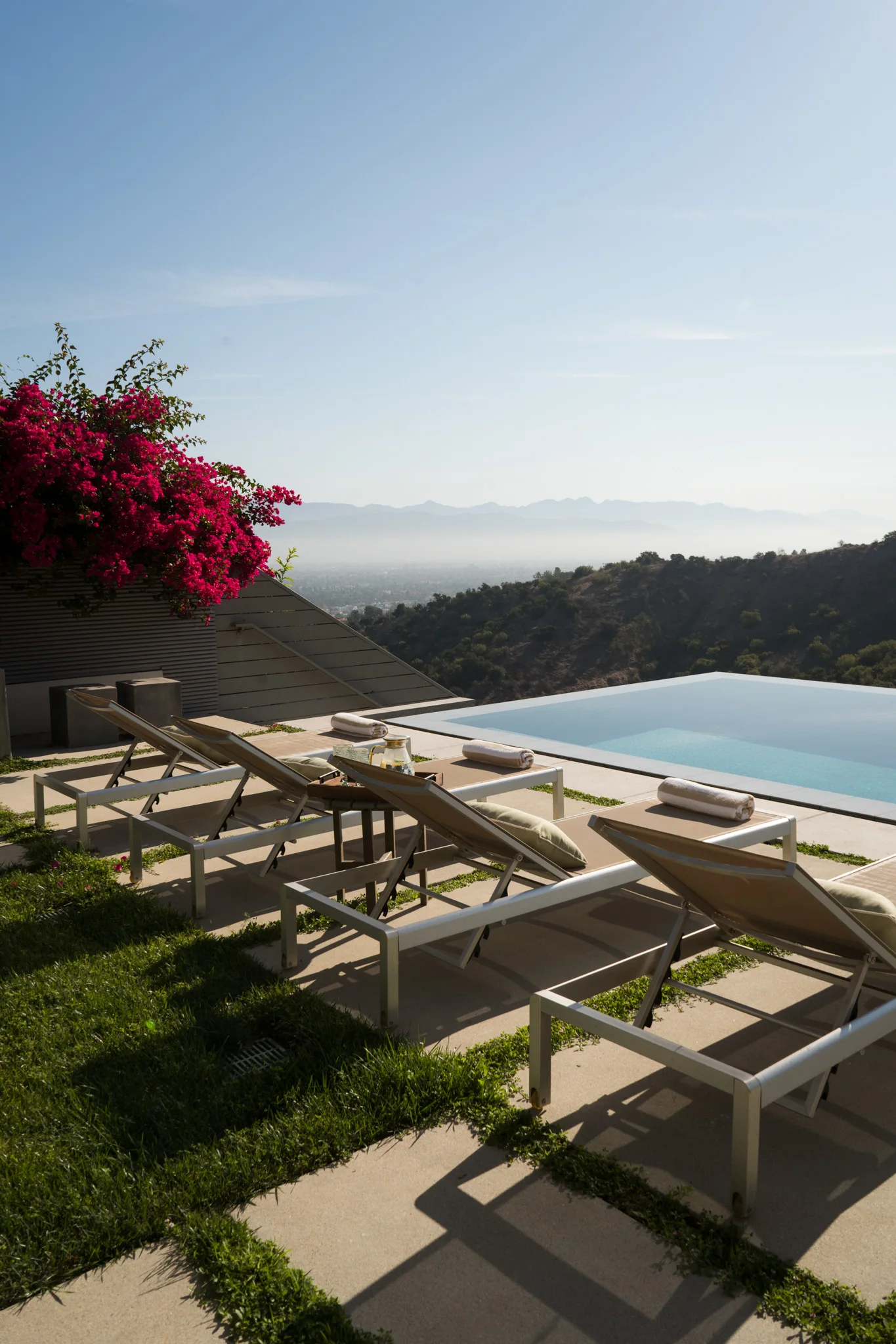 Loungers at the infinity edge, bougainvillea overhanging the water and the coast far in the distance