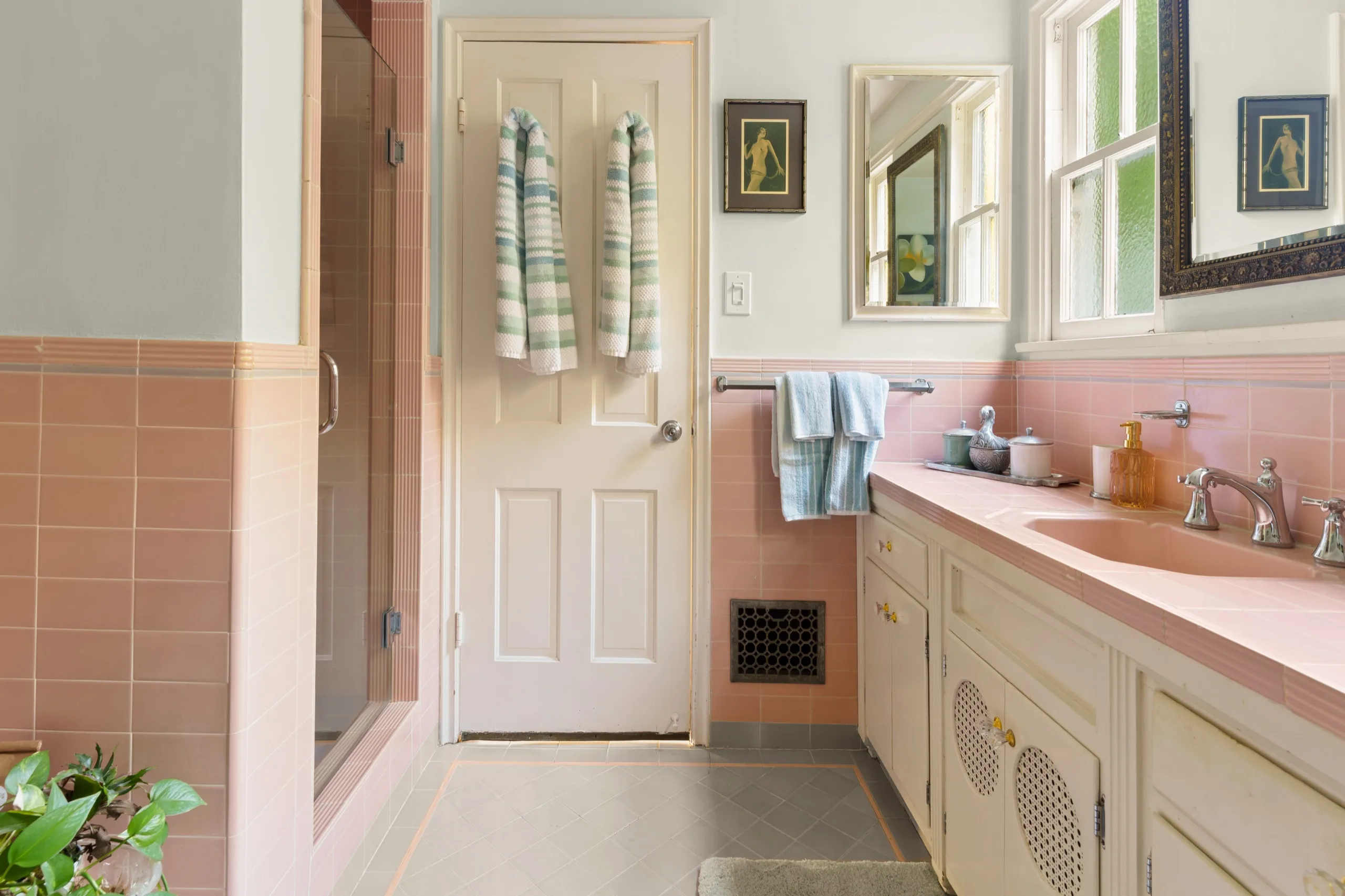 Period bathroom tiled in pink, double vanity below the window and a glazed shower alongside