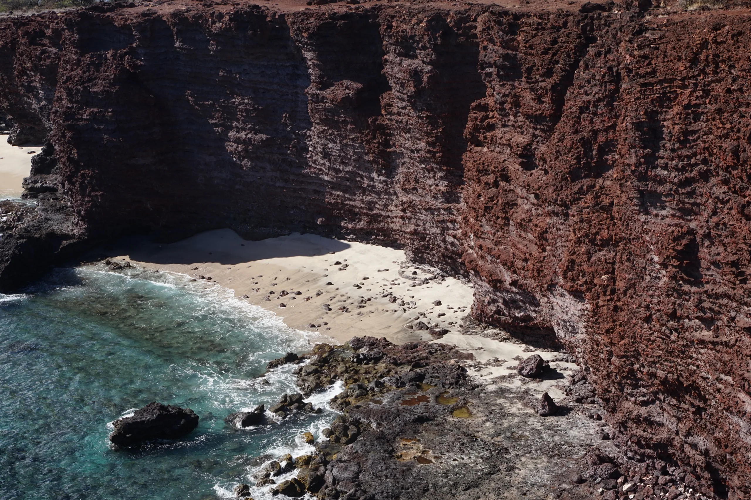 Hidden crescent of sand at the foot of towering red volcanic cliffs