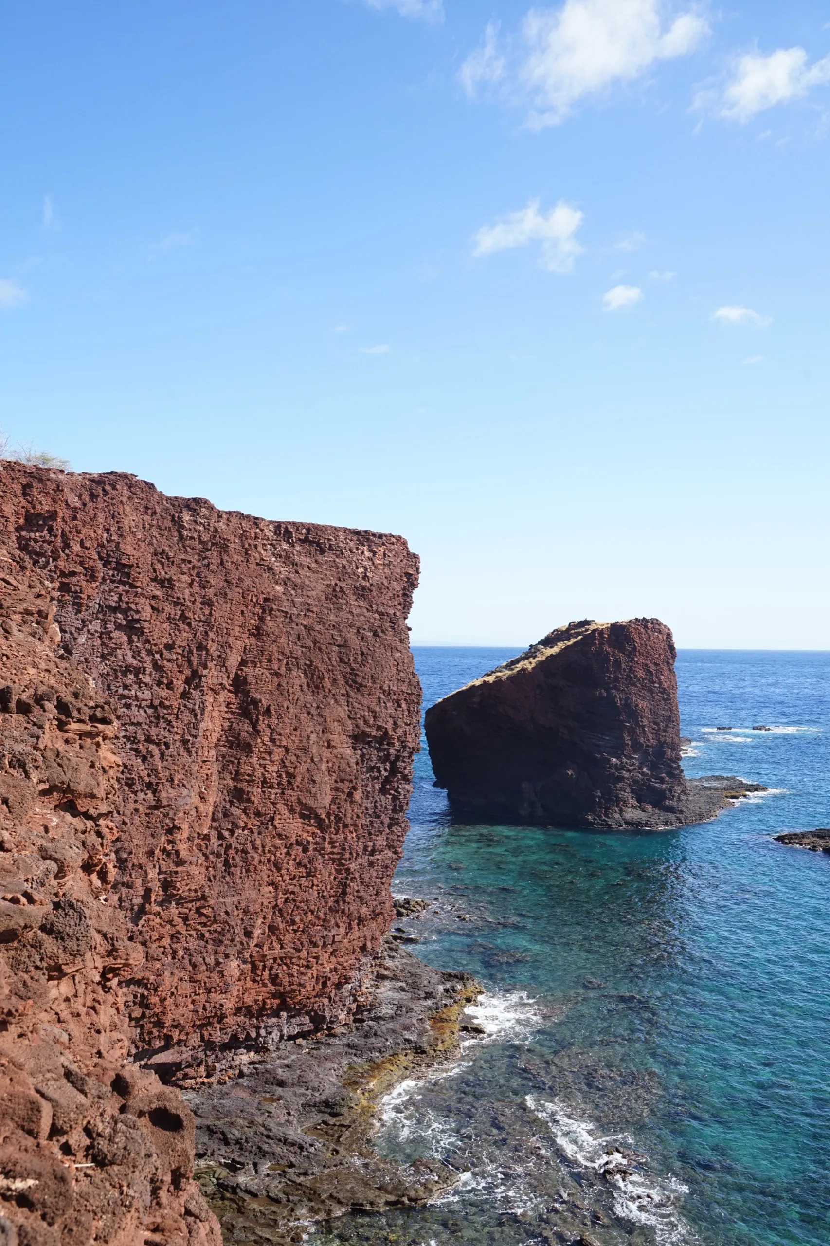 Sweetheart Rock standing offshore from rust-red sea cliffs, clear turquoise water below