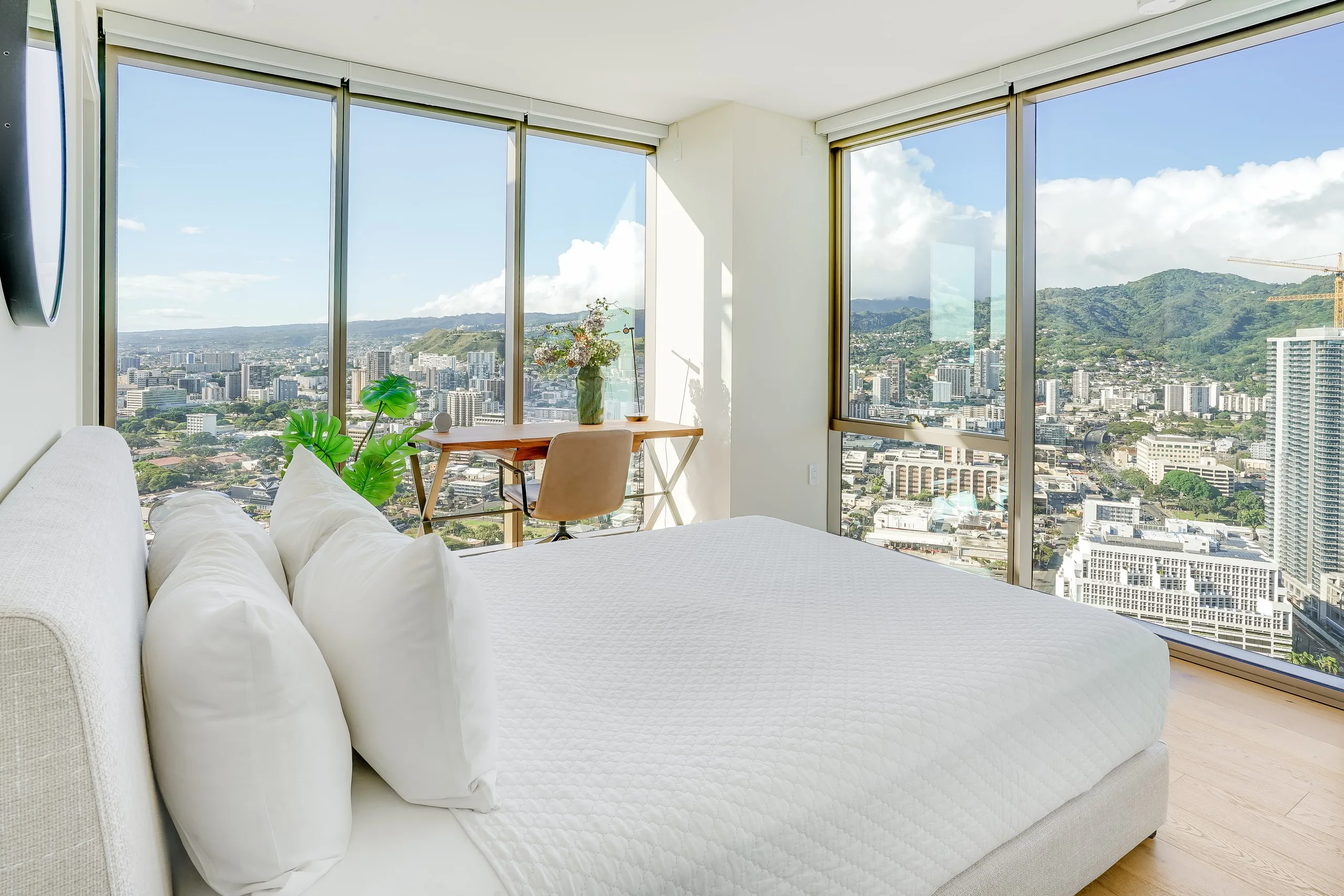High-floor bedroom in white linen, two walls of glass over the city to the mountains beyond