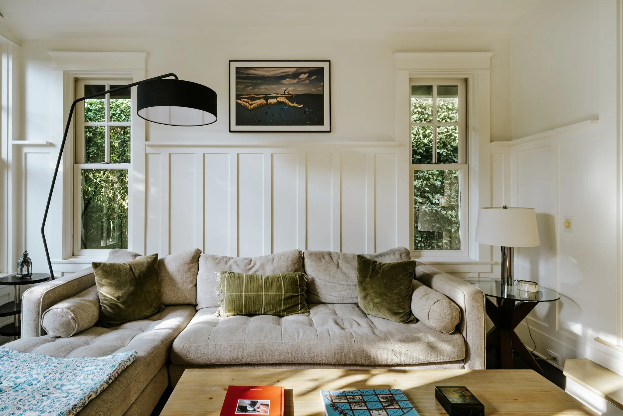 Living room in white board-and-batten, deep linen sofa under an arc lamp between two sash windows