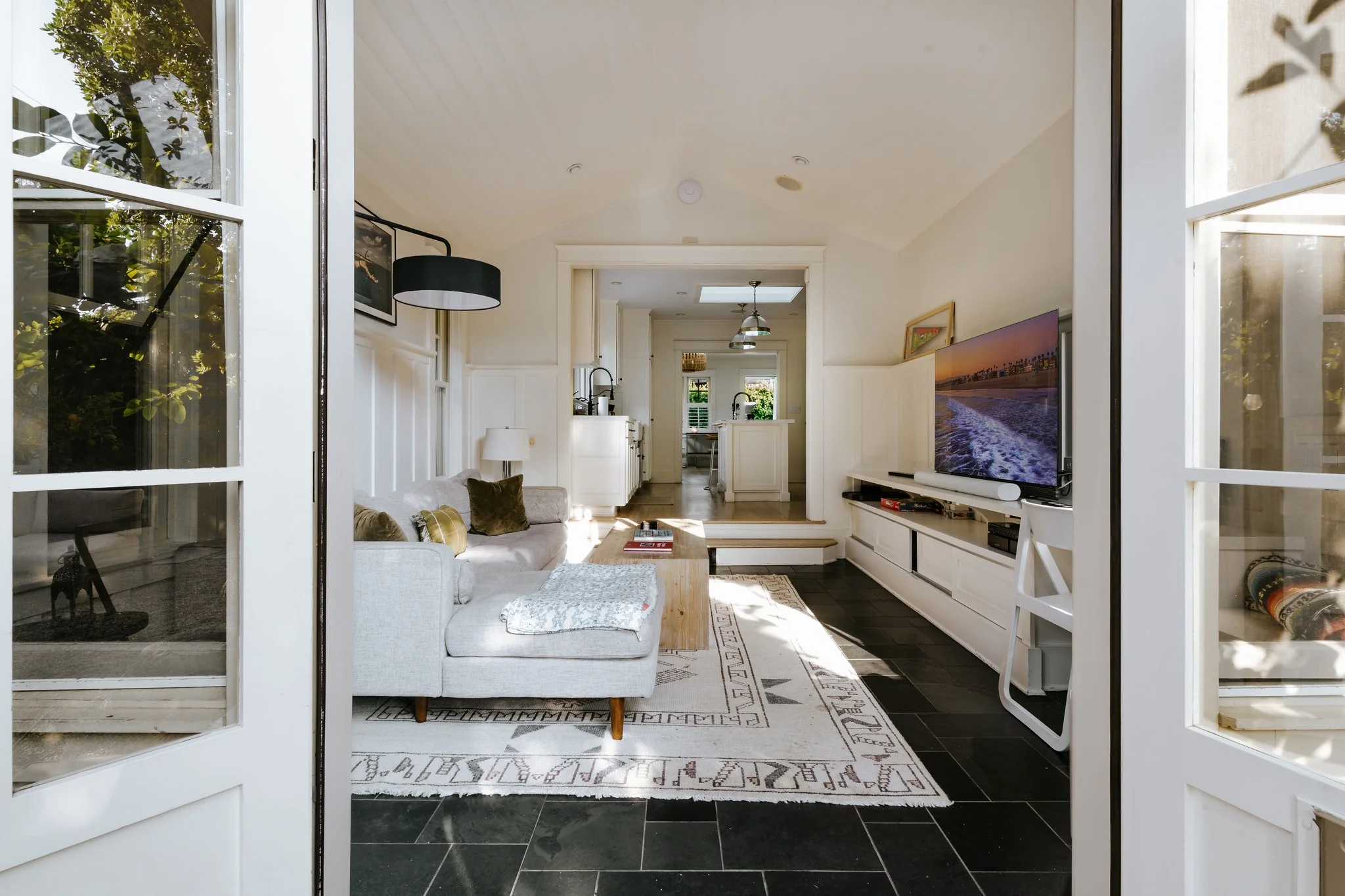 The living room seen from the garden through open French doors, slate floor running out to the deck