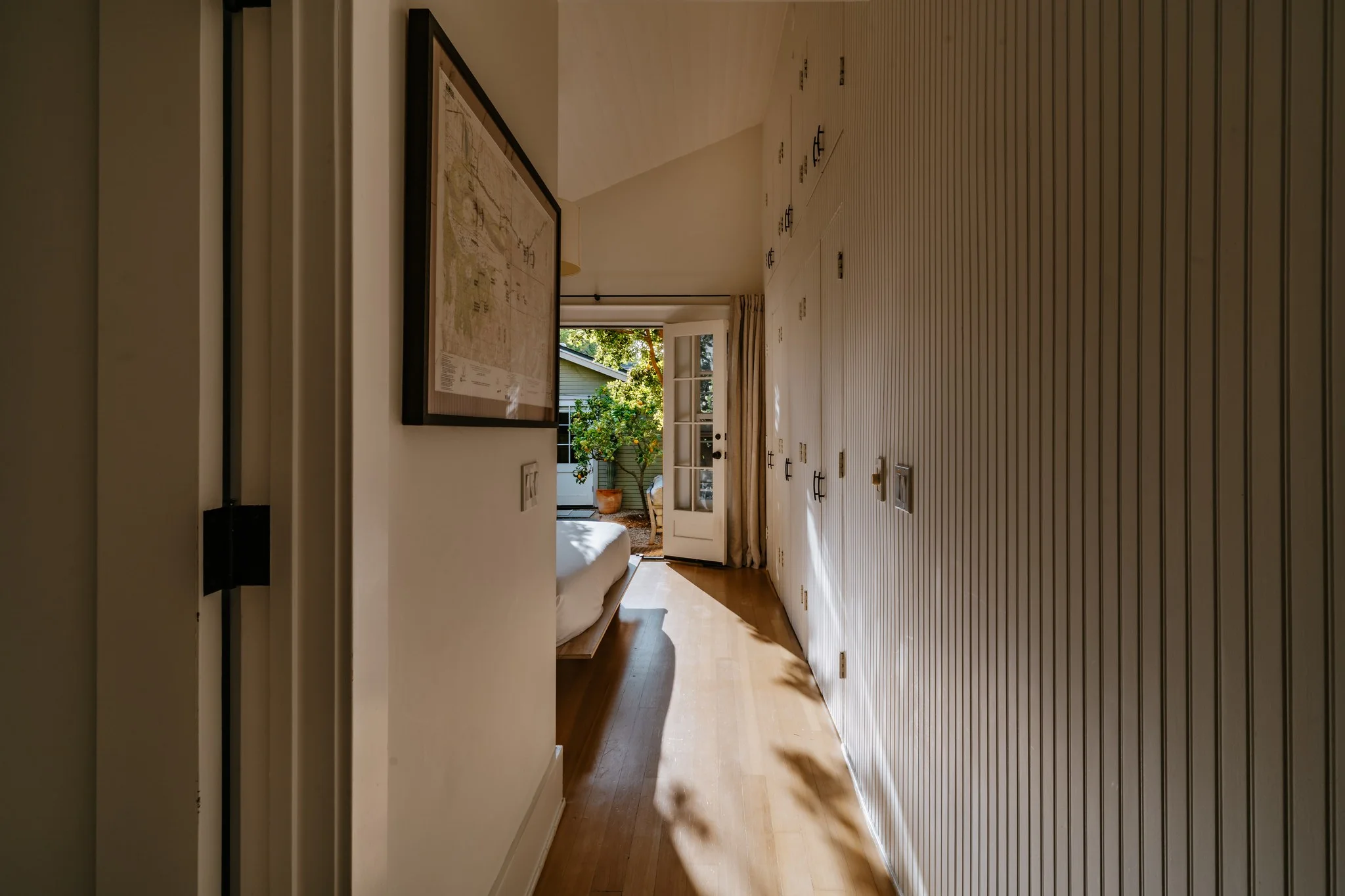 Hallway lined in narrow vertical boards, light from an open door at the far end across the oak floor