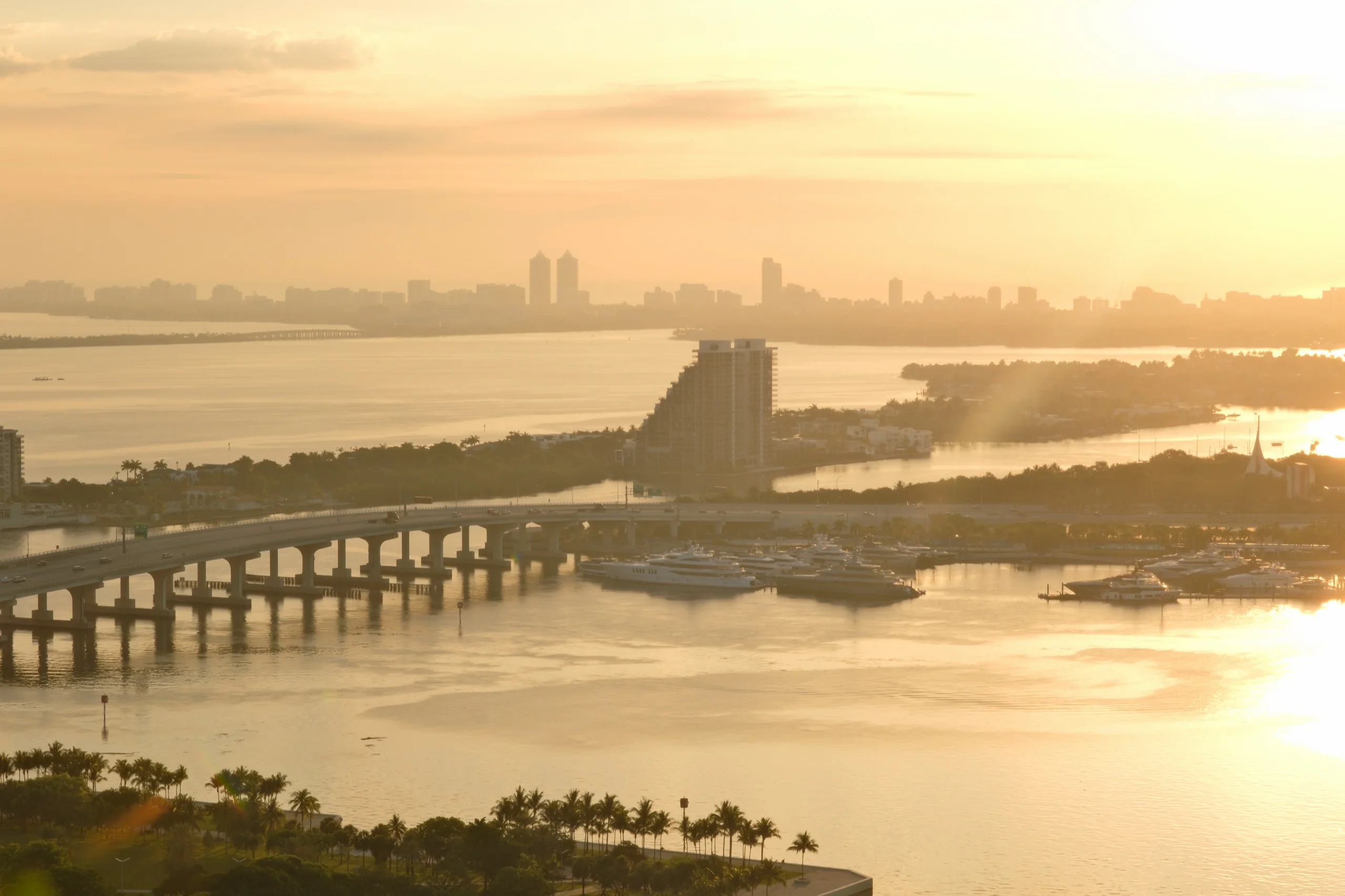 Aerial over Biscayne Bay at sunset, causeways threading between the islands in low gold haze