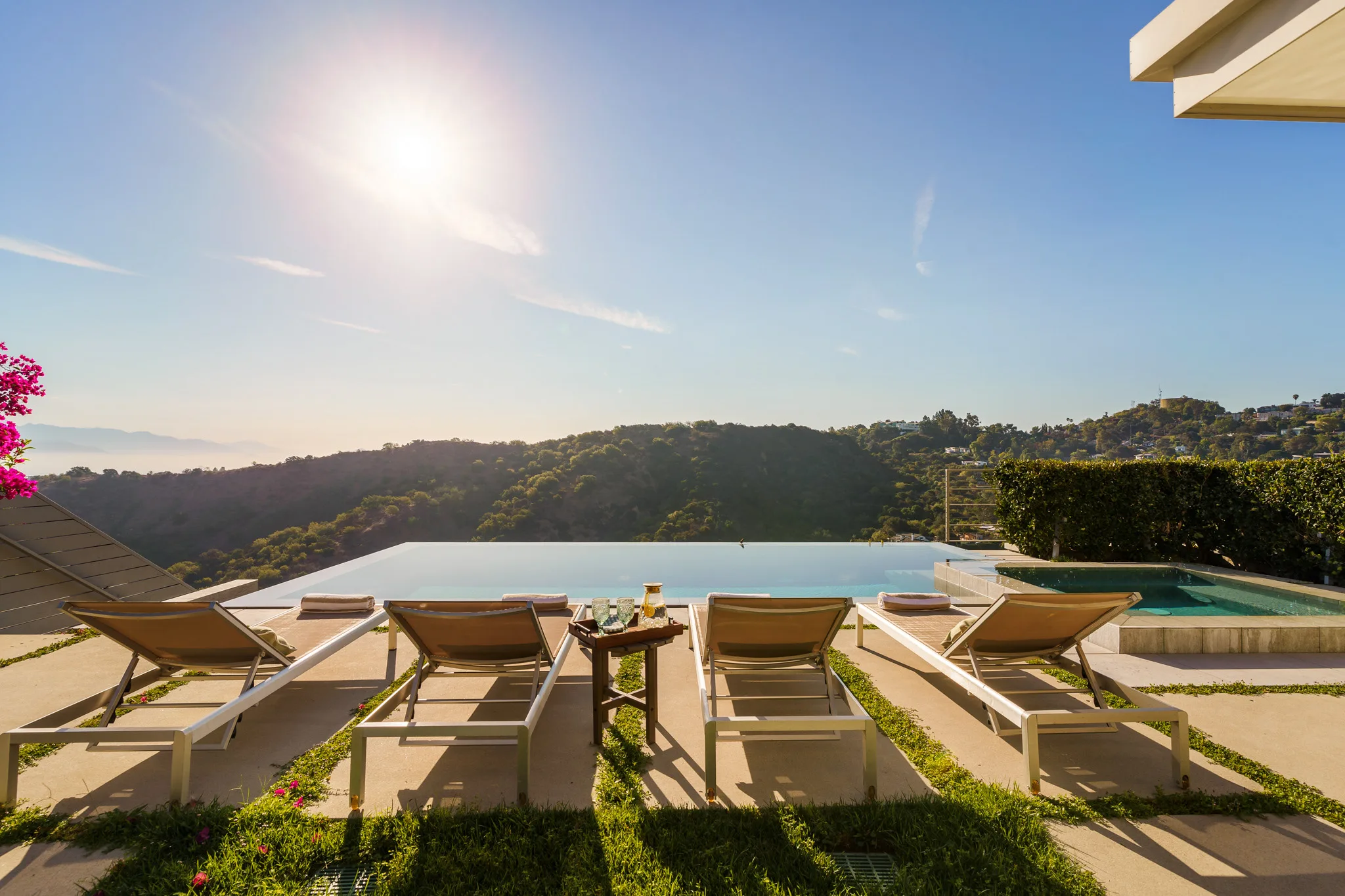 Infinity pool and teak loungers on a hillside terrace, low sun over wooded canyon ridges beyond