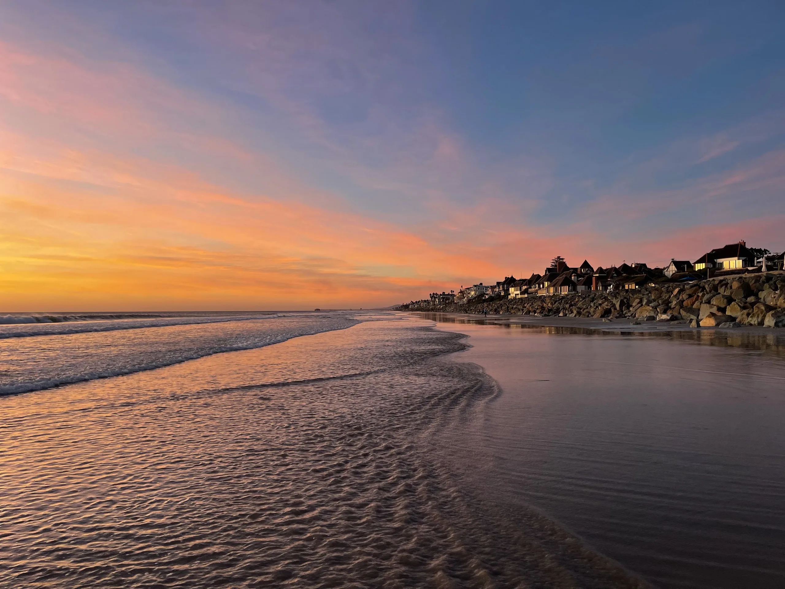 Low tide at sunset, wet sand mirroring a pink sky, beach houses along the rocks beyond