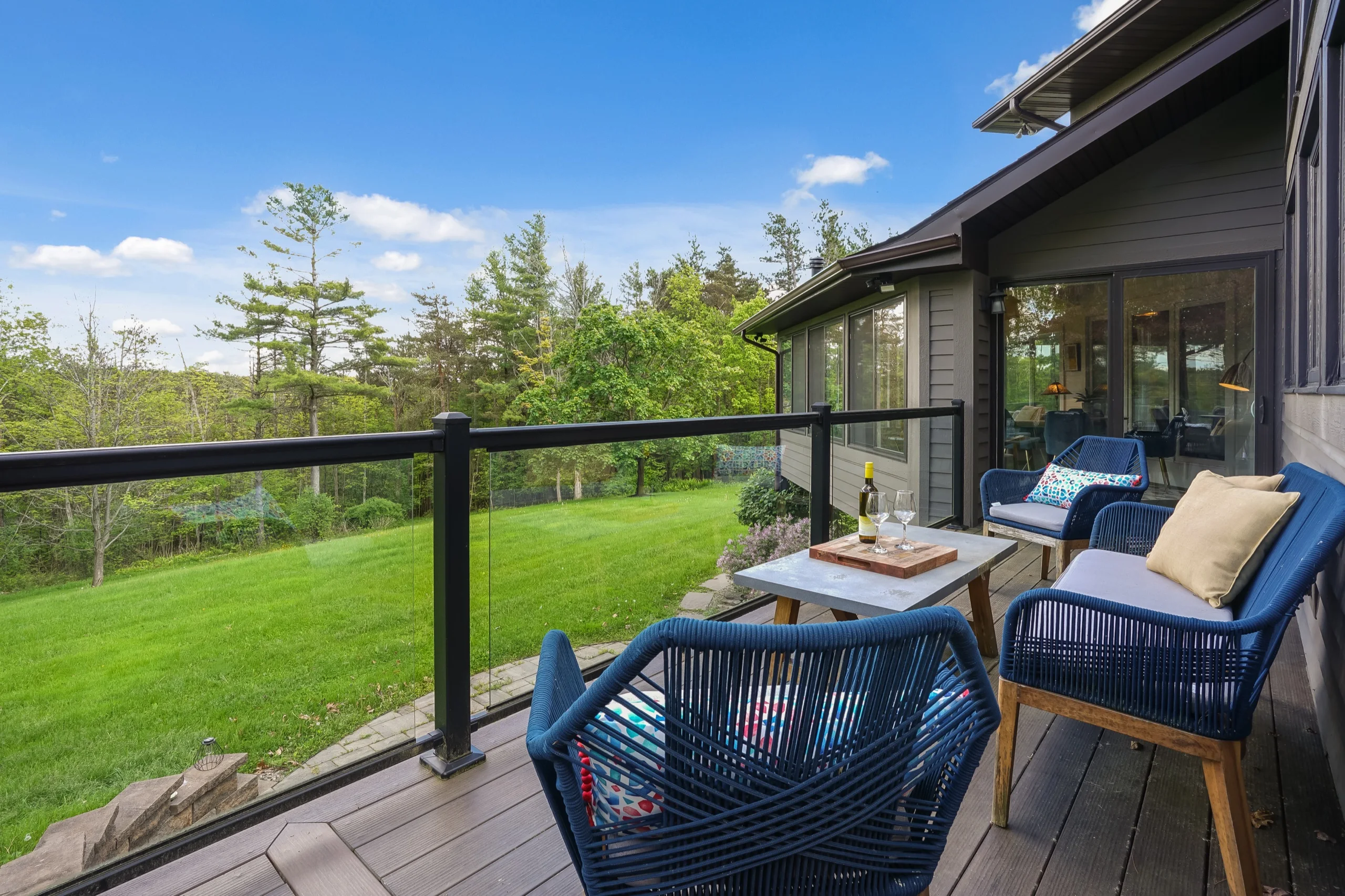 Deck seating in blue wicker above a wide lawn, white pines closing the view