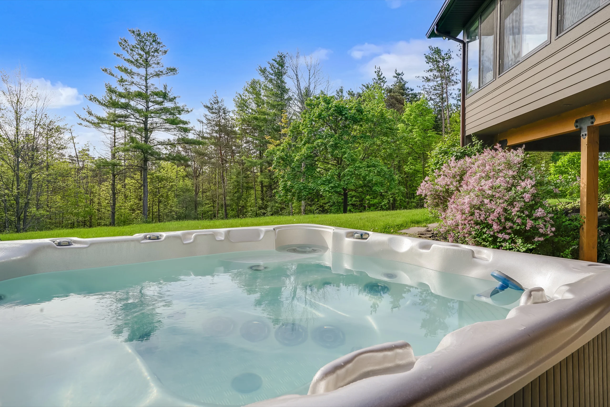 Hot tub at the edge of the lawn, lilac and white pines standing behind it