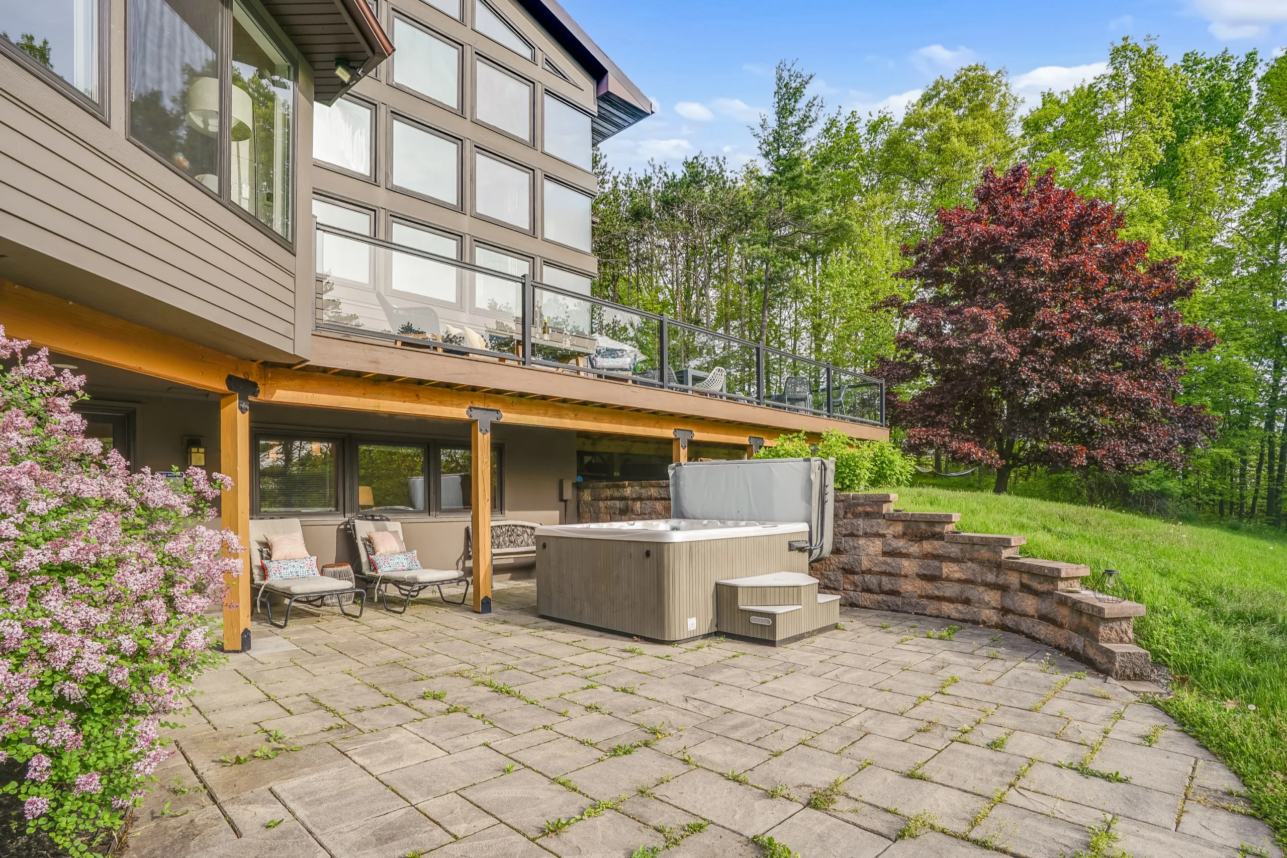 Flagstone patio below the house with a hot tub against a stone retaining wall, lilac in flower